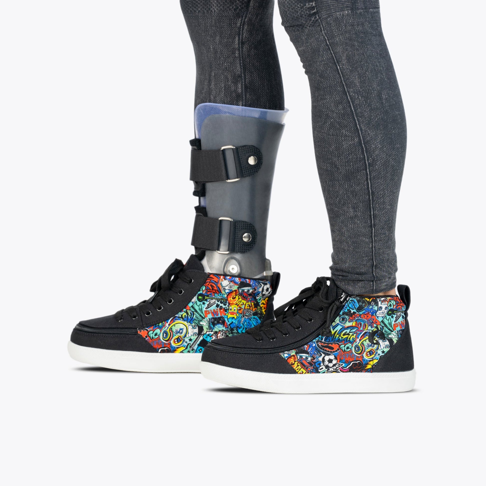 A person wears black jeans, a prosthetic leg with a black and silver brace, and BILLY Footwear’s Night Sk8ter BILLY Classic D|R II High—colorful graffiti-style high-tops designed for AFO-friendliness, style, and all-day comfort.